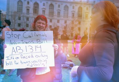 a scan of a color photo of a person holding a sign about an anti trans law that a Republican in California is trying to pass