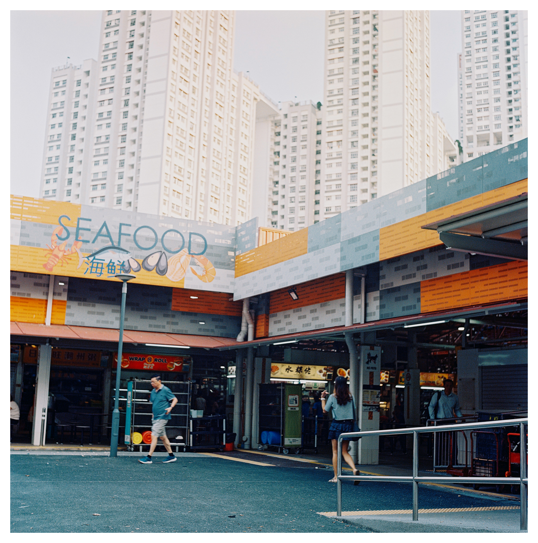 A scan of a medium format square color photo of a wet market in Singapore with tall buildings behind it