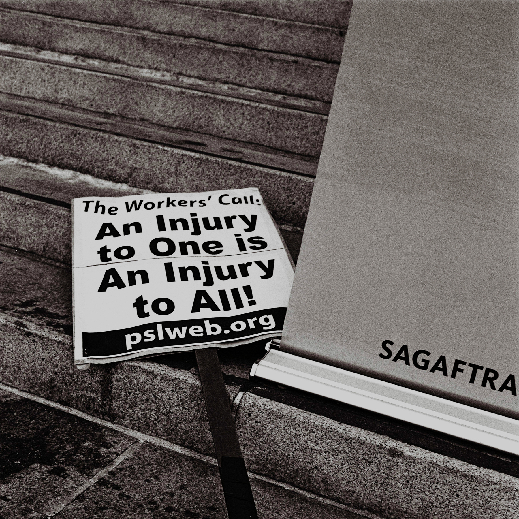 a scan of a black and white photo showing a placard that says PSL (a socialist party), injury to one is an injury to all next to a SAG-AFTRA sign