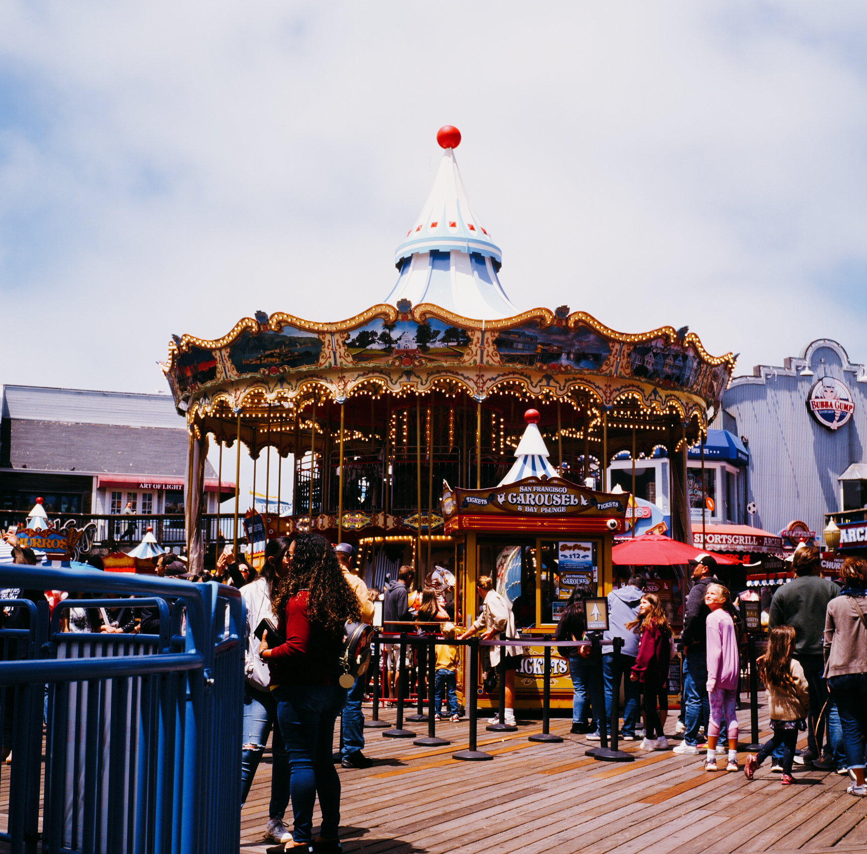 a scan of a color slide photo of a tourist atraction in san francisco. many people are standing in line for the carousel ride