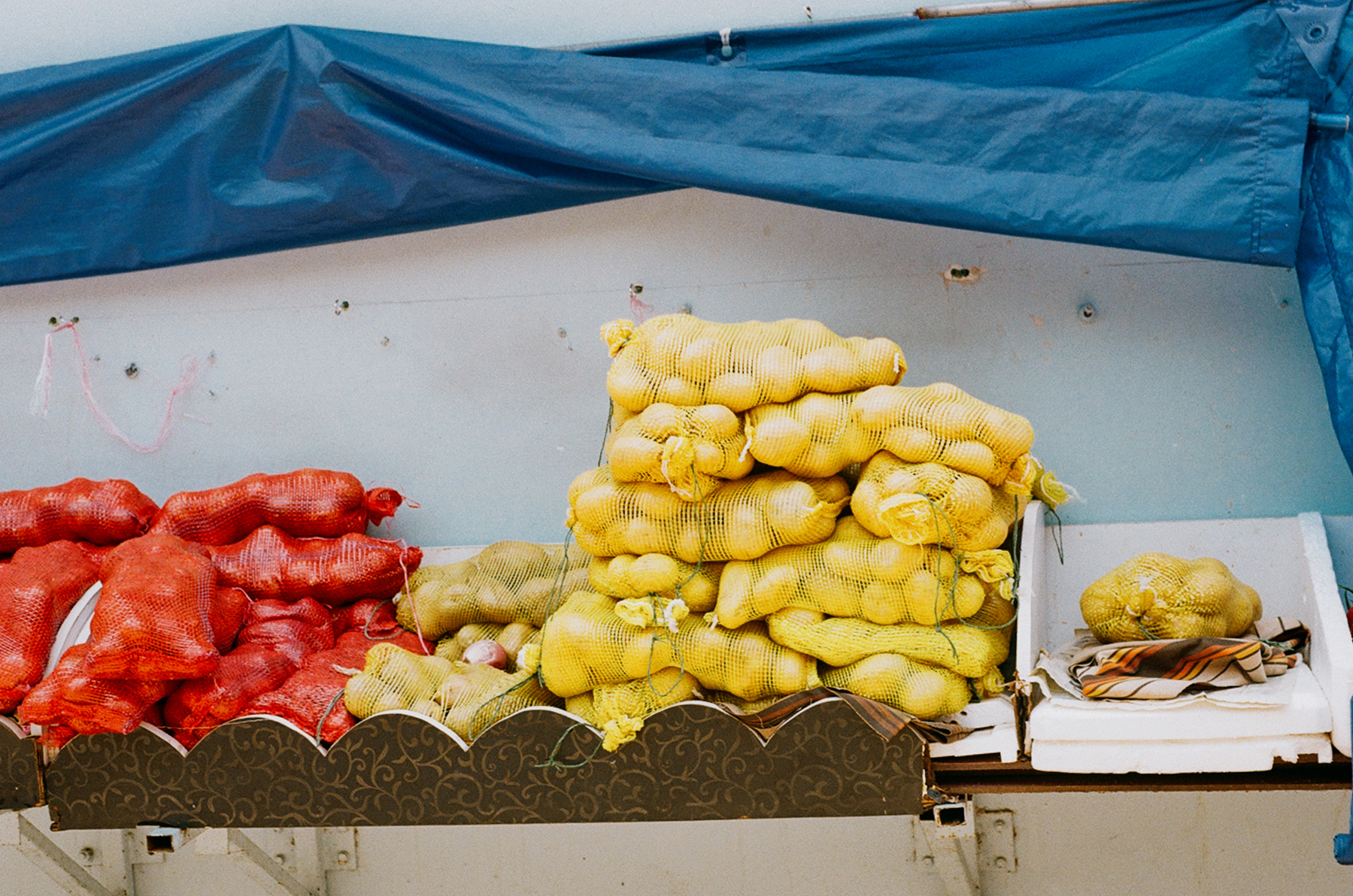 3. A scan of onions and potatoes being displayed at a little India grocer with a blue tarp over it
