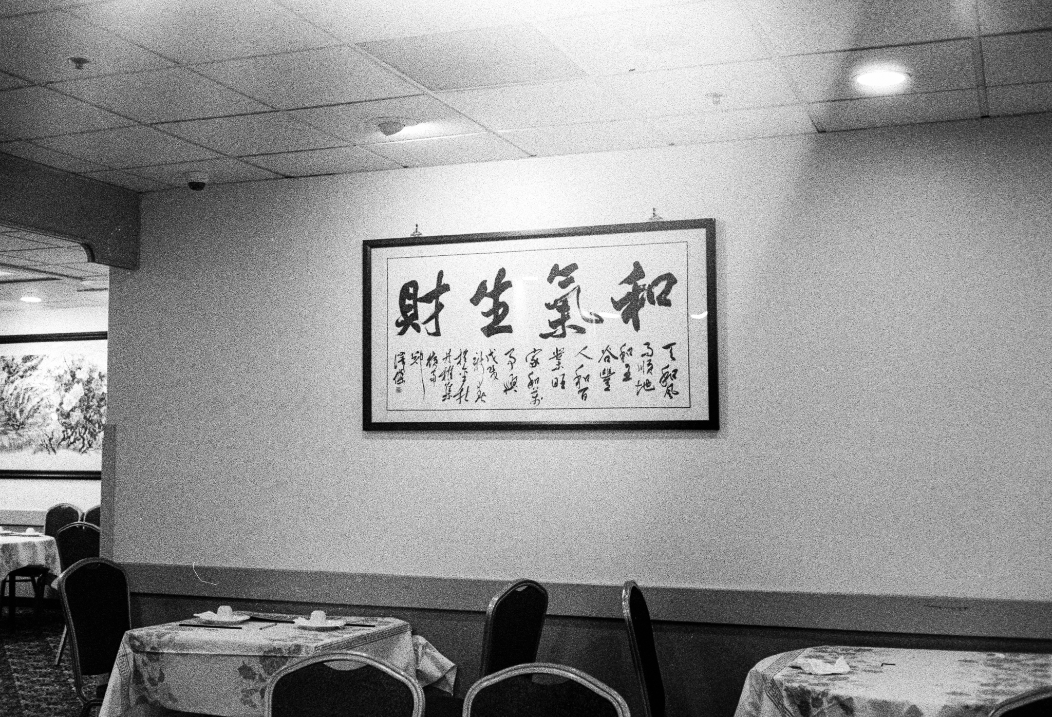 A scan of a black and white photograph of some Chinese calligraphy writing on a wall in a Chinese restaurant in Oakland, California