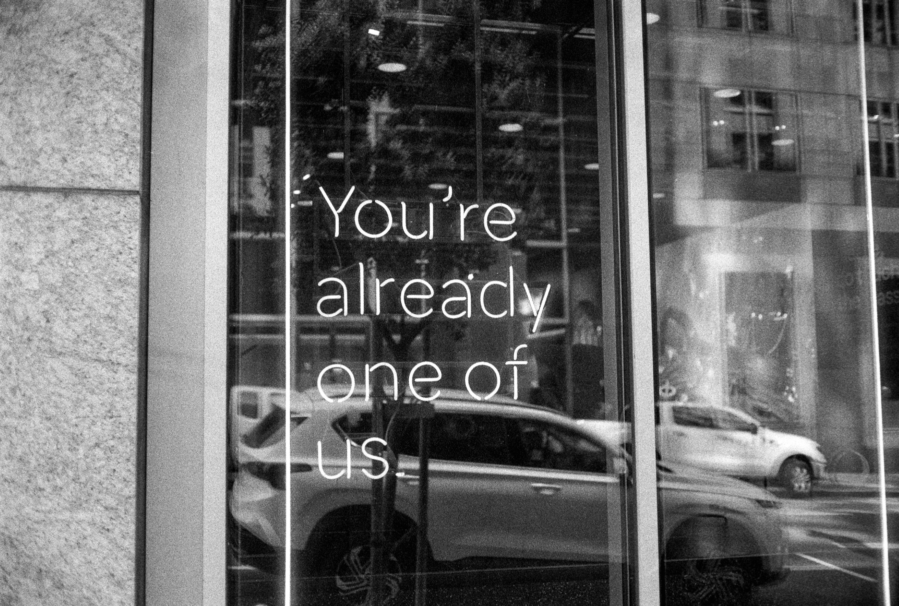 a scan of a black and white photo showing a neon sign that says You're Already One Of Us