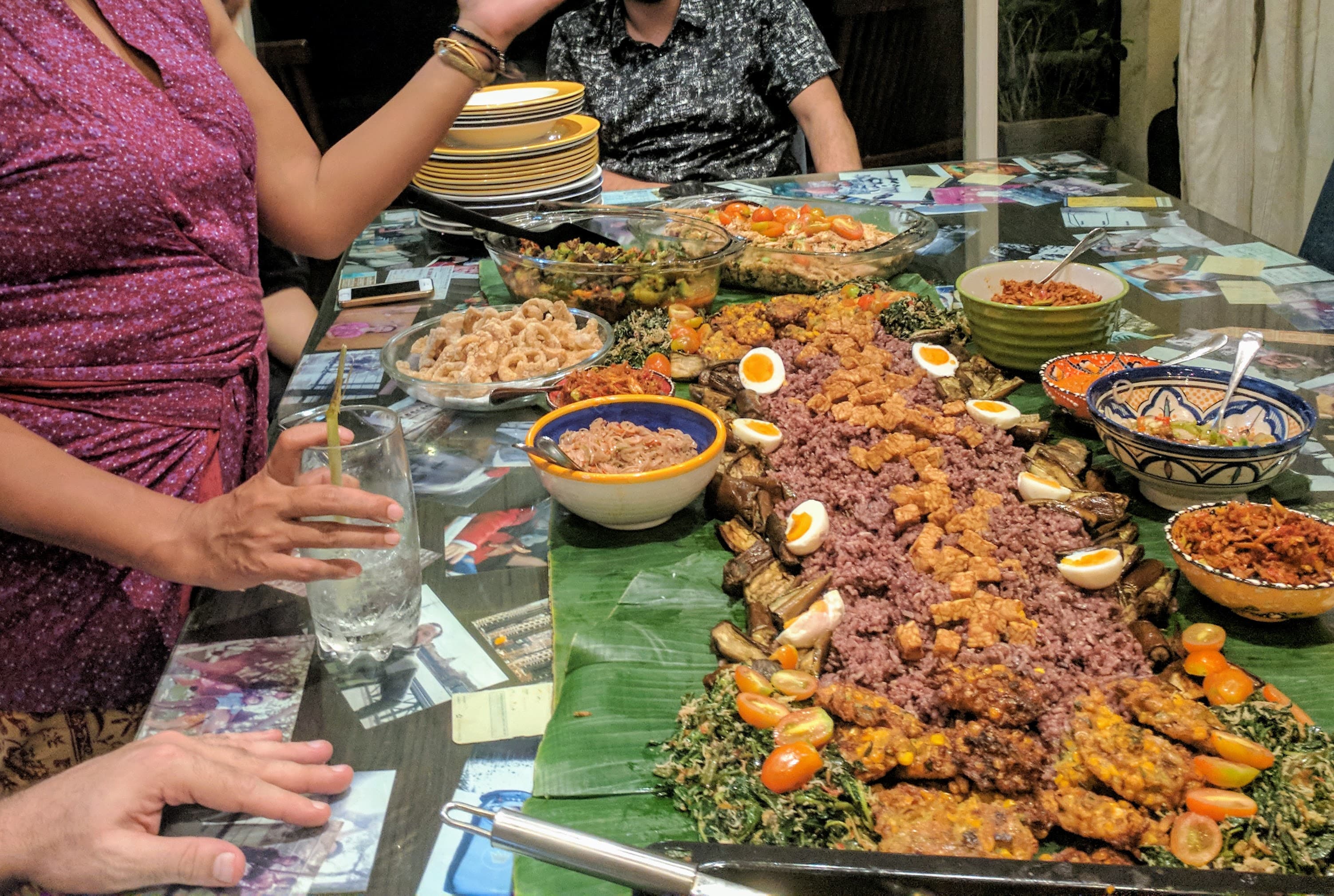 A photo of a person hovering over a large banana leaf full of Indonesian food with many colors