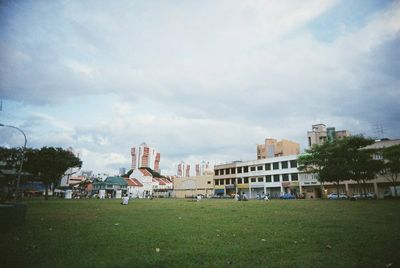 a scan of a color photo of grass and dark blue sky in a low lit photo, with buildings in the background