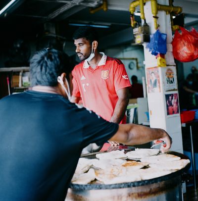 A scan of a color photo of a roti prata seller in Singapore