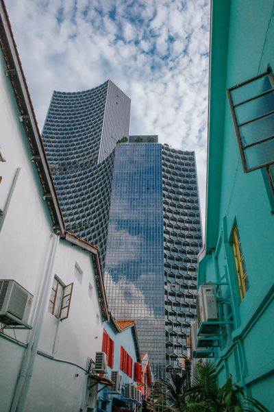 a color photo showing a narrow alleyway between two historic short buildings leading towards a tall and modern hotel in the background