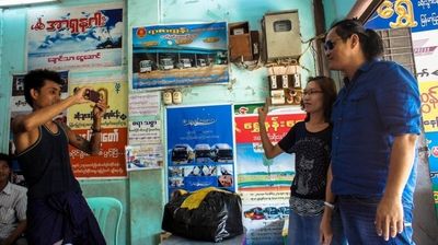 a color photograph of a person taking a photo for a local couple in a Burmese bus station