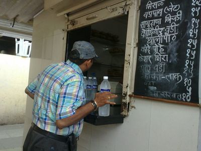 a photo of a man standing at a window of a Alibag vada pav restaurant in India