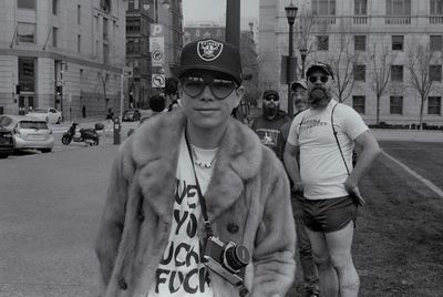 a scan of a black and white photo of a person wearing heart-shaped sunglasses and having a Pentax film camera around their neck