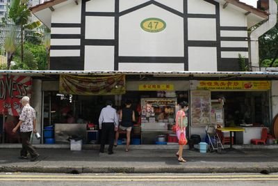 a color photograph of an old neighborhood in Singapore with people walking past food sellers in a low rise building