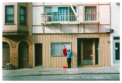 a scan of a color photo showing a Chinese man holding up a piece of cloth over the exterior of a building