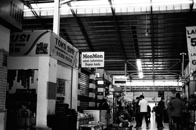 a scan of a black and white photo of the interior of a wet market in indonesia, showing many shops with indonesian signs