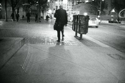 a scan of a black and white photograph of a person walking down a street in downtown San Francisco, there are streaks of light around the film negative scan