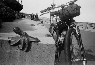 A scan of a black and white photograph of a octopus sculpture that looks like it's sat on the corner of the ledge. a bicycle leaning next to it