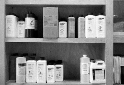 a scan of a black and white photo showing some film development chemicals on a shelf in a photography store, brands include Ilford and Kodak