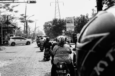 a scan of a black and white photo of traffic in surabaya from the back of a motorbike, pillion. in front, several motorbikes and their passengers stopped at traffic
