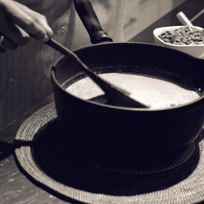 A black and white photo of a cast iron cauldron with milk in it, and someone stirring