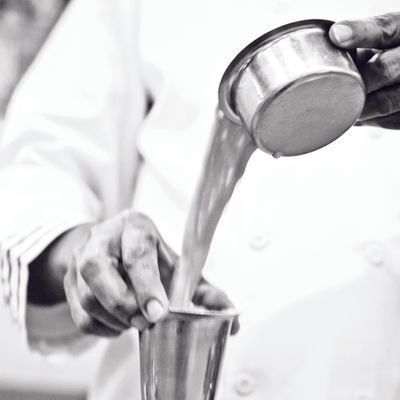 A black and white photo of someone pouring milk from Indian-style steel cups