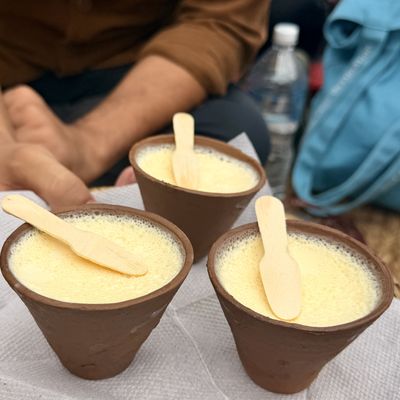 Three brown clay cups filled with a pale, frothy drink, with a wooden spoon resting in each