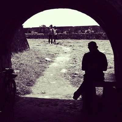 A black and white photo of a man sitting at a bench under a circular arch