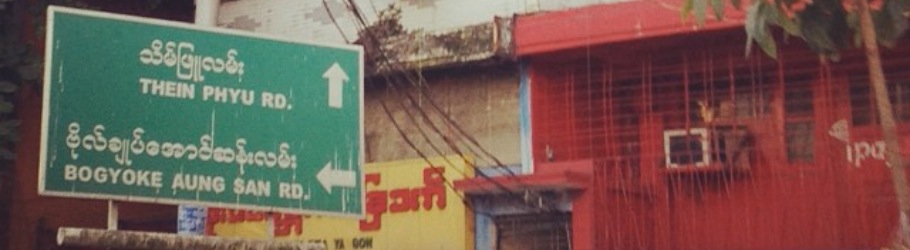 Street scene in Yangon with traffic, buildings, and overhead wires.
